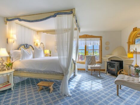 A room showcases a four poster bed with views of the valley and a fireplace.
