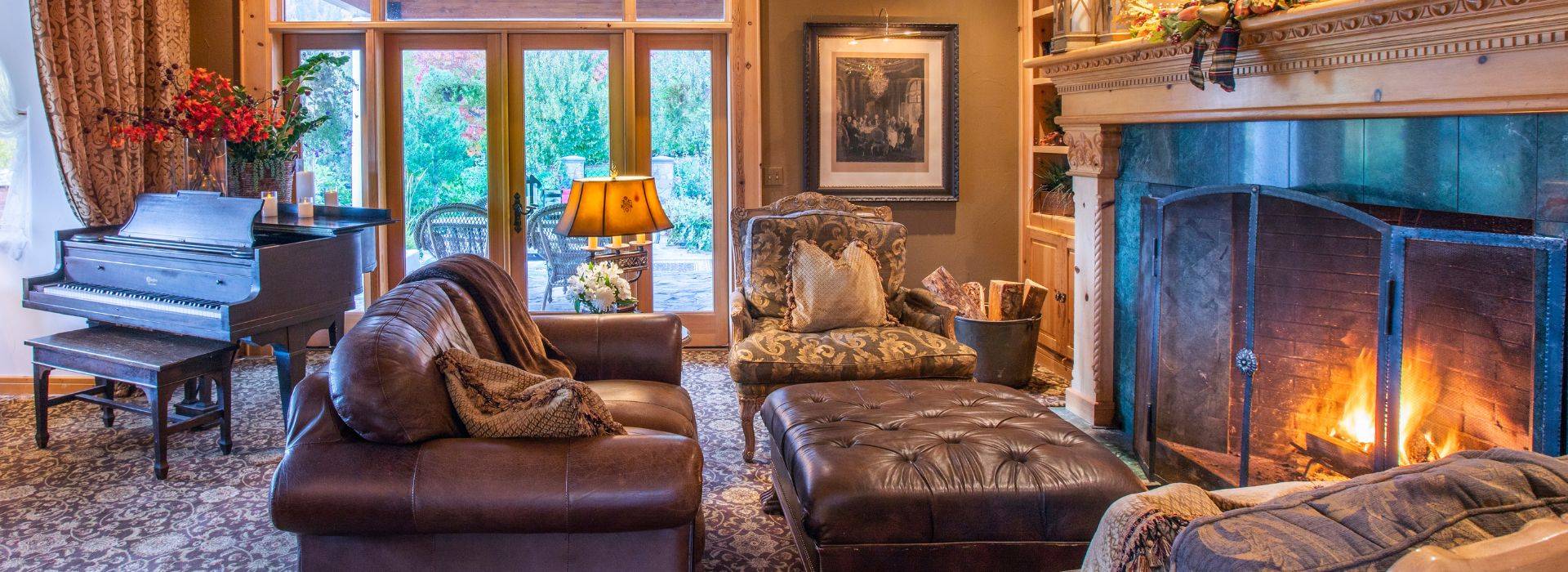 Luxurious living room with leather couch, sitting chairs in front of fireplace, piano by large windows and patio doors